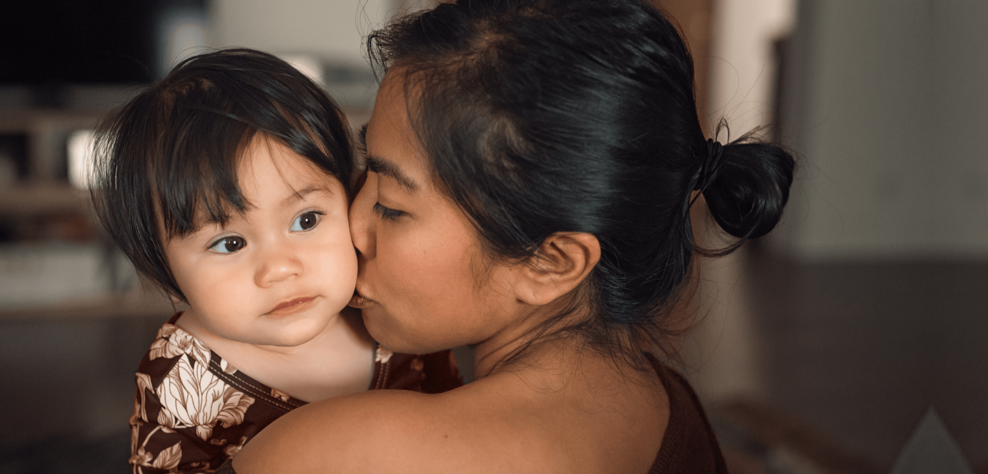 Photo of a woman kissing a toddler on the cheek.